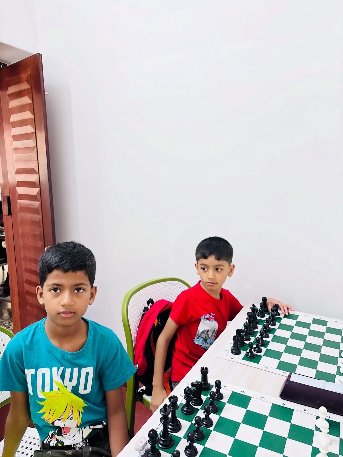 Young chess students seated beside academy practice boards